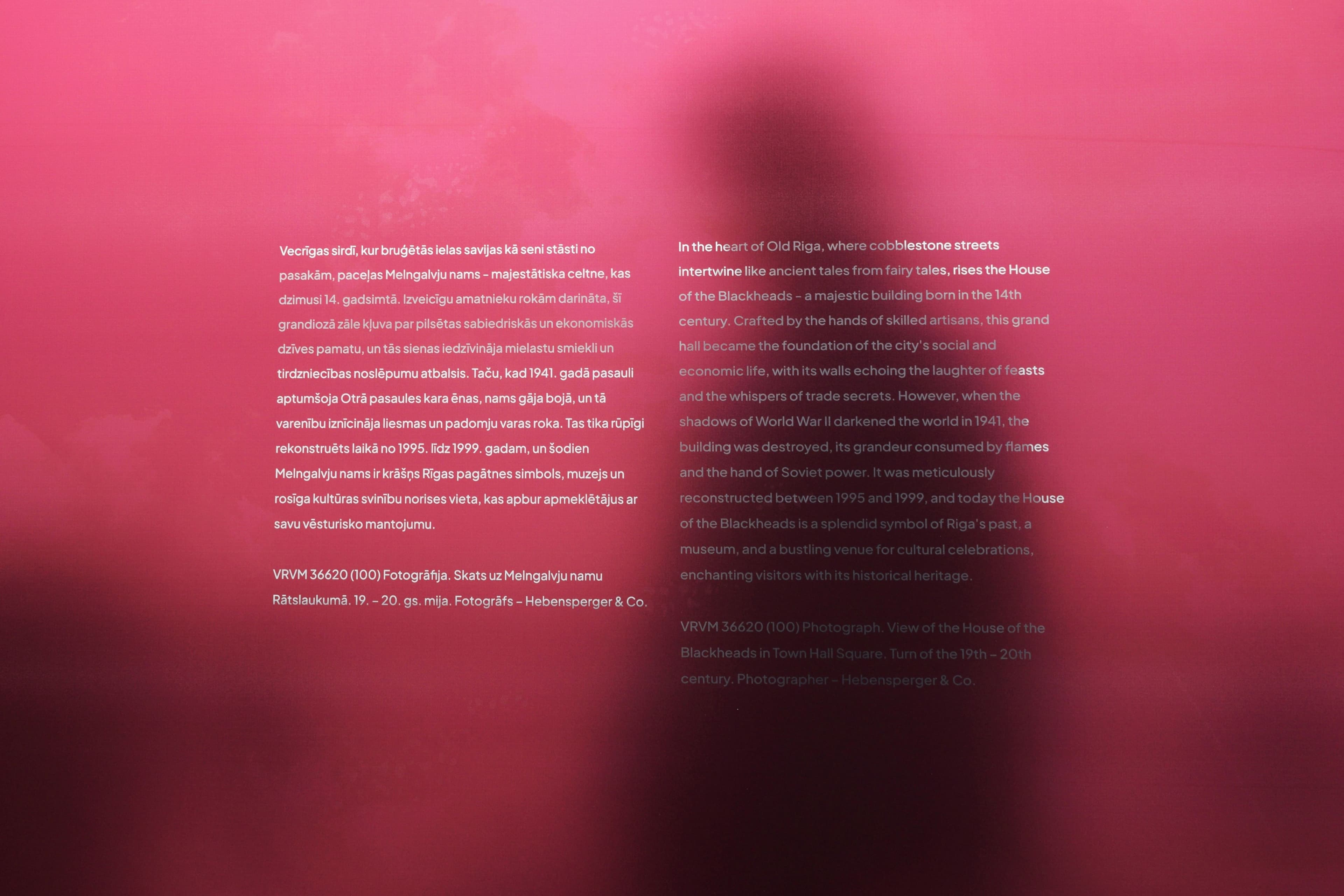 Text in two columns on red background wall and a shadow of a person behind the wall